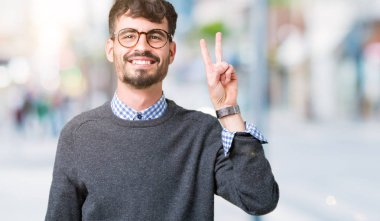 Genç yakışıklı akıllı adam izole arka plan üzerinde gözlük giyen gösteren ve emin ve mutlu gülümserken parmaksayısı iki ile işaret.