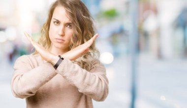 Sweatershirt izole arka plan ret ifade geçiş kollarına eksi işareti, kızgın surat yapıyor giyen genç güzel sarışın kadın