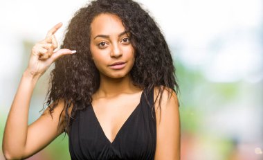 Kıvırcık saçlı Genç güzel kız görünümlü moda etek gülümseyen ve kendine güvenen, el ile boyutu işareti yaparken parmaklar ve kamera bakıyor. Ölçü kavramı.