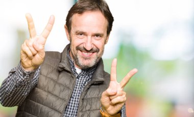 Zafer işareti yapıyor parmak gösterilen kamera seyir gülümseyen orta yaş yakışıklı adam giyen kış yelek. İki numaralı.