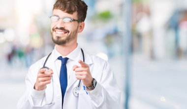 Genç doktor adam, mutlu ve komik yüz ile kamera parmakları işaret izole arka plan üzerinde hastane ceket giyiyor. İyi enerji ve Vibes.