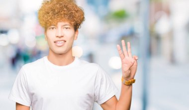 Gösterilen ve parmakları ile işaret casual beyaz t-shirt giyen afro saçlı Genç yakışıklı adam kendinden emin ve mutlu gülümseyerek iken üçüncü.