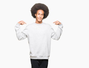 Yüzünde gülümseme ile kendinden emin görünüyorsun, kendini gururlu ve mutlu parmakları ile işaret sportif sweatshirt giyen afro saçlı genç Afro-Amerikan adam.