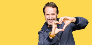 Orta yaş yakışıklı adam aşk kalp sembolü ve elleri ile şekil gösteren gülümseyen bir ceket giyiyor. Romantik kavram.