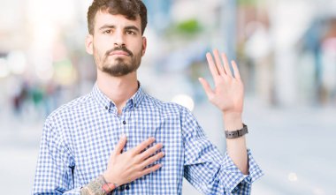 İzole arka plan üzerinde genç yakışıklı iş adamı el ile göğüs ve açık palmiye, bir sadakat vaat yemini yapmak ile küfür