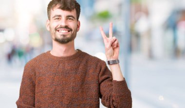 Gösterilen arka plan üzerinde kış kazak giyen genç yakışıklı adam izole ve parmakları ile işaret kendinden emin ve mutlu gülümseyerek ise ikinci.