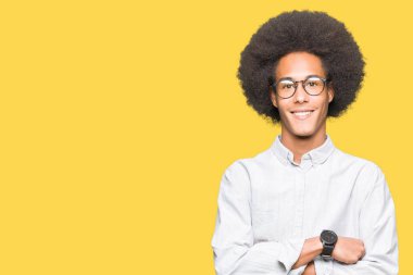 Afrikalı-Amerikalı genç afro saçlı gözlük mutlu yüz çapraz silah kameraya bakarak ile gülümseyen giyiyor. Olumlu bir kişi.