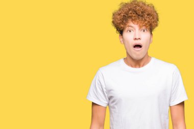 Korkuyor ve şok sürpriz ifade, korku ve heyecan yüz ile rahat beyaz t-shirt giyen afro saçlı Genç yakışıklı adam.