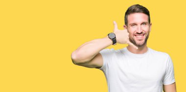 Yakışıklı adam rahat beyaz t-shirt giyen gülümseyen el ve parmak telefonda konuşmak ile telefon jest yapıyor. Kavramları iletişim.
