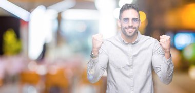 Yakışıklı delikanlı izole arka plan kutlama üzerinde güneş gözlüğü takıyor şaşırttı ve başarı için kaldırdı kollarını açarak hayret ve gözleri açık. Kazanan kavramı.