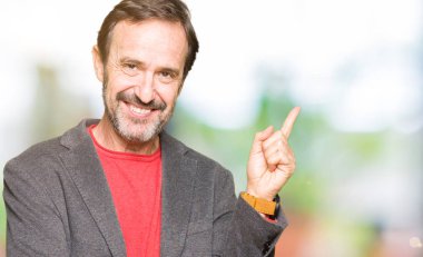 Kameraya bakarak yan el ve parmak ile işaret orta yaş yakışıklı iş adamı yüzünde kocaman bir gülümseme ile.