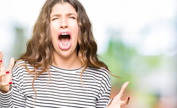 Young beautiful woman wearing stripes sweater crazy and mad shouting and yelling with aggressive expression and arms raised. Frustration concept.