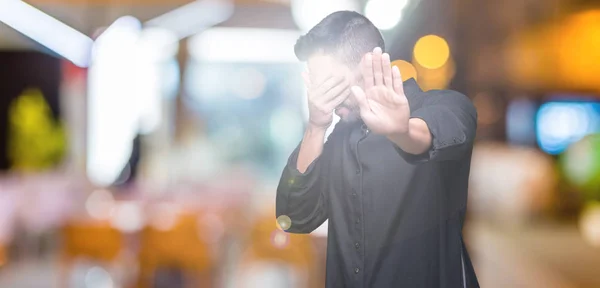 Young Christian priest over isolated background covering eyes with hands and doing stop gesture with sad and fear expression. Embarrassed and negative concept.