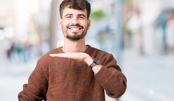 İzole arka plan eller eller büyük gösterilen ve büyük boy işareti, ölçü birimi sembolü ile üzerinde kış kazak giyen genç yakışıklı adam. Kameraya bakarak gülümsüyordu. Ölçüm kavramı.