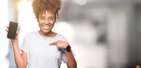 Young african american woman showing smartphone screen over isolated background with surprise face pointing finger to himself
