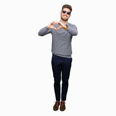 Genç yakışıklı adam aşık kalp simgesi ve elleriyle şekil gösteren gülümseyen güneş gözlüğü takıyor. Romantik kavramı.