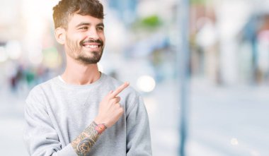 İzole arka neşeli bir gülümseme ile el ve parmak kadar yan yüzünde mutlu ve doğal ifade ile işaret yüz üzerinden sweatshirt giyen genç yakışıklı adam