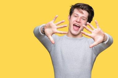 Gösterilen arka plan üzerinde kış kazak giyen genç yakışıklı adam izole ve parmakları ile işaret kendinden emin ve mutlu gülümseyerek süre on numara.