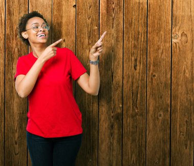 Güzel genç Afro-Amerikan kadın gülümseyerek ve iki elleri ve parmakları ile tarafına işaret kamera bakarak izole arka plan üzerinde gözlük.