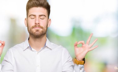 Genç yakışıklı iş adamı rahatla ve gülümseyen gözlerle kapalı parmak jestle meditasyon yapıyor. Yoga kavramı.