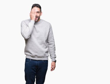 El yüz ve sürpriz duygu kendinden emin gülümseme ile tek gözüyle kapsayan izole arka plan üzerinde sweatshirt giyen genç yakışıklı adam.