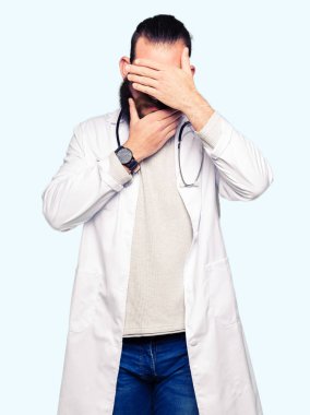 Tıbbi kat kaplama gözler ve ağız el ile giyen sakallı genç sarışın doktor adam şaşırttı ve şok. Duygu gizleme