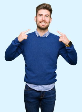 Kendinden emin gösterilen ve işaret parmakları diş ve ağız ile gülümseyen genç yakışıklı iş adam. Sağlık kavramı.