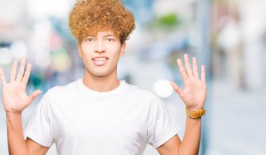 Gösterilen ve parmakları ile işaret casual beyaz t-shirt giyen afro saçlı genç yakışıklı adam kendinden emin ve mutlu gülümseyerek süre on numara.