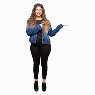 Gözlük ve hayrete ve el ile sunulması ve parmak ile işaret ederken kameraya gülümseyen denim ceket giyen genç güzel kadın.