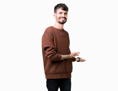 Açık el ile doğal gülümseyen girmek için izole arka plan davet üzerine kış kazak giyen genç yakışıklı adam