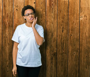 Diş ağrısı veya dişlerde dişlerle ilgili hastalık nedeniyle ağız acı ifadesi ile el ile dokunmak izole arka plan üzerinde gözlük güzel genç Afro-Amerikan kadın. Diş hekimi kavramı.