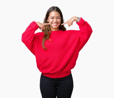 Kendinden emin gösterilen ve işaret parmakları diş ve ağız ile gülümseyen izole arka plan üzerinde kırmızı kış kazak giyen genç güzel esmer kadın. Sağlık kavramı.