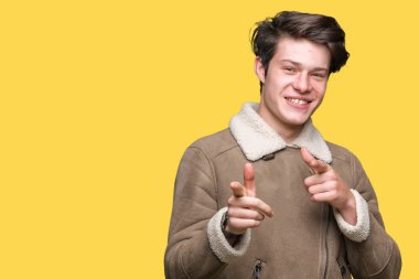 Üzerinde kış ceket giyen genç yakışıklı adam arka plan fotoğraf makinesi ile mutlu ve komik yüz için parmakları işaret izole. İyi enerji ve vibes.