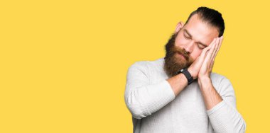 Kapalı gözleri ile gülümseyen iken rahat kazak uyku yorgun rüya ve eller ile poz giyen genç sarışın adam.