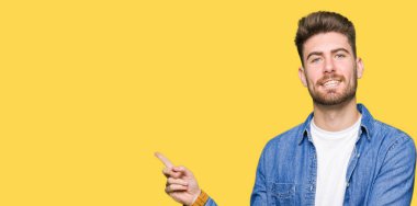 Kameraya bakarak yan el ve parmak ile işaret yüzünde, kocaman bir gülümseme ile rahat denim ceket giyen genç sarışın yakışıklı.