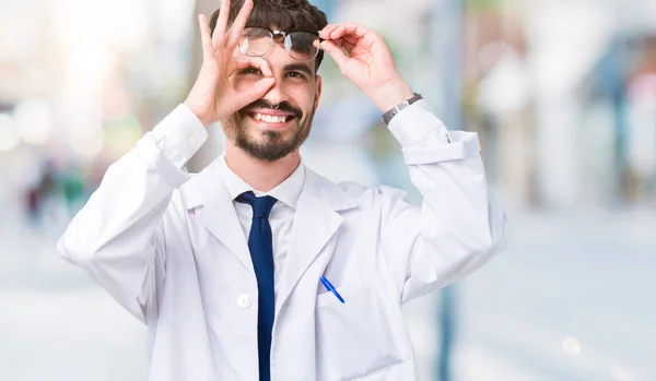 年轻的专业科学家男子穿着白色外套在孤立的背景做确定的手势与手微笑 眼睛通过手指看与愉快的面孔 — 图库照片