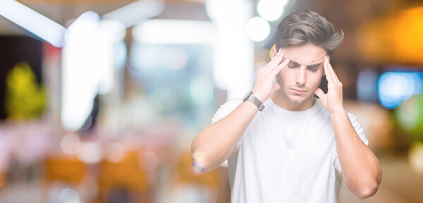 Young handsome man wearing white t-shirt over isolated background with hand on head for pain in head because stress. Suffering migraine.