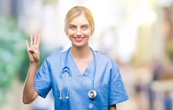 年轻美丽的金发医生外科医生护士妇女在孤立的背景显示和指向与手指第四 同时微笑着自信和快乐 — 图库照片
