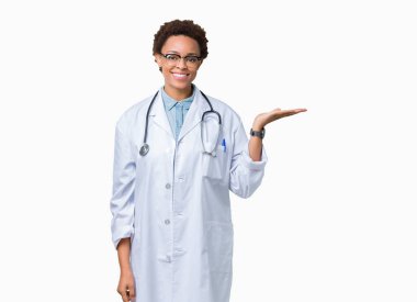 Neşeli sunulması ve kameraya bakarak avucunun ile işaret gülümseyen izole arka plan üzerinde tıbbi ceket giyen genç Afro-Amerikan doktor kadın.