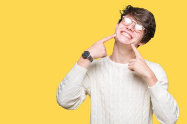 Kendinden emin gösterilen ve işaret parmakları diş ve ağız ile gülümseyen izole arka plan üzerinde gözlük takan yakışıklı delikanlı. Sağlık kavramı.