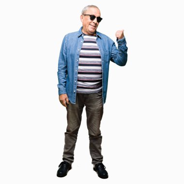 Denim ceket ve seyir ve başparmak yanında yukarıyı mutlu yüz ile gülümseyen güneş gözlüğü takan yakışıklı komuta sizde.