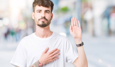 Arka plan üzerinde beyaz t-shirt giyen genç yakışıklı adam izole göğüs ve bir sadakat sözü yemin yapma avuç, el ile küfür