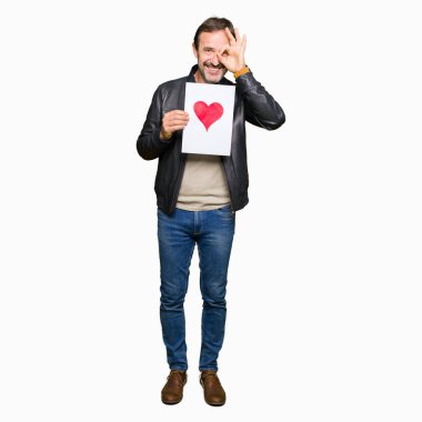 Yakışıklı orta yaş adam mutlu yüz ile kırmızı kalp ile kağıt tutarak gözler parmaklarıyla görünümlü el ile ok işareti yapıyor gülümseyen