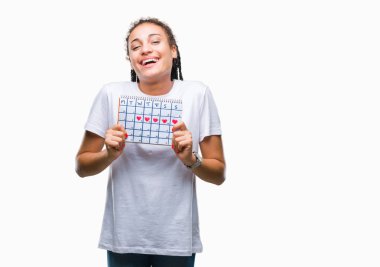 Genç örgülü saç Afrikalı Amerikalı kız, mutlu bir yüz ayakta ve kendine güvenen bir gülümseme ile gülümseyen dişler gösteren izole arka plan üzerinde menstruasyon takvimi tutarak