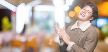 İzole arka plan üzerinde kış ceket giyen genç yakışıklı adam alkışlar ve mutlu ve neşeli alkışlar, gülümseyen gururlu eller birlikte