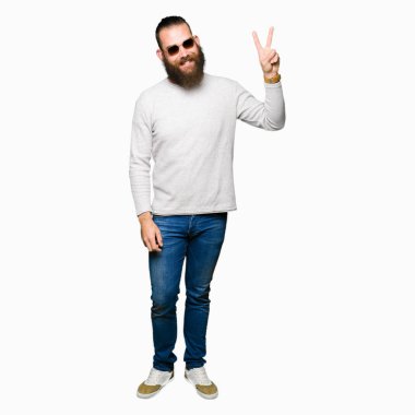 Genç hipster adam mutlu yüz zafer işareti yaparken kameraya göz kırpıyor ile gülümseyen güneş gözlüğü takıyor. İki numaralı.