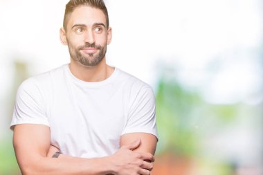 Genç giyiyor rahat beyaz t-shirt görünümlü yan ve dik dik bakma uzağa düşünce gülümseyen izole arka plan üzerinde adam..