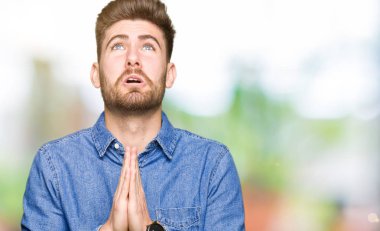 Casual kot gömlek yalvarıyor ve umut ifade yüzünde çok duygusal ve endişe ile birlikte elleriyle dua giyen genç yakışıklı sarışın adam. Bağışlanmak. Din kavramı.