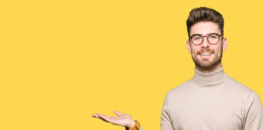 Neşeli sunulması ve kameraya bakarak avucunun ile işaret gülümseyen gözlüklü genç yakışıklı iş adamı.