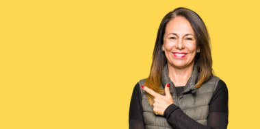 Yüze mutlu ve doğal ifade ile yan kadar el ve parmak ile işaret yüz bir gülümseme ile neşeli kış yelek giyen güzel orta yaş kadın